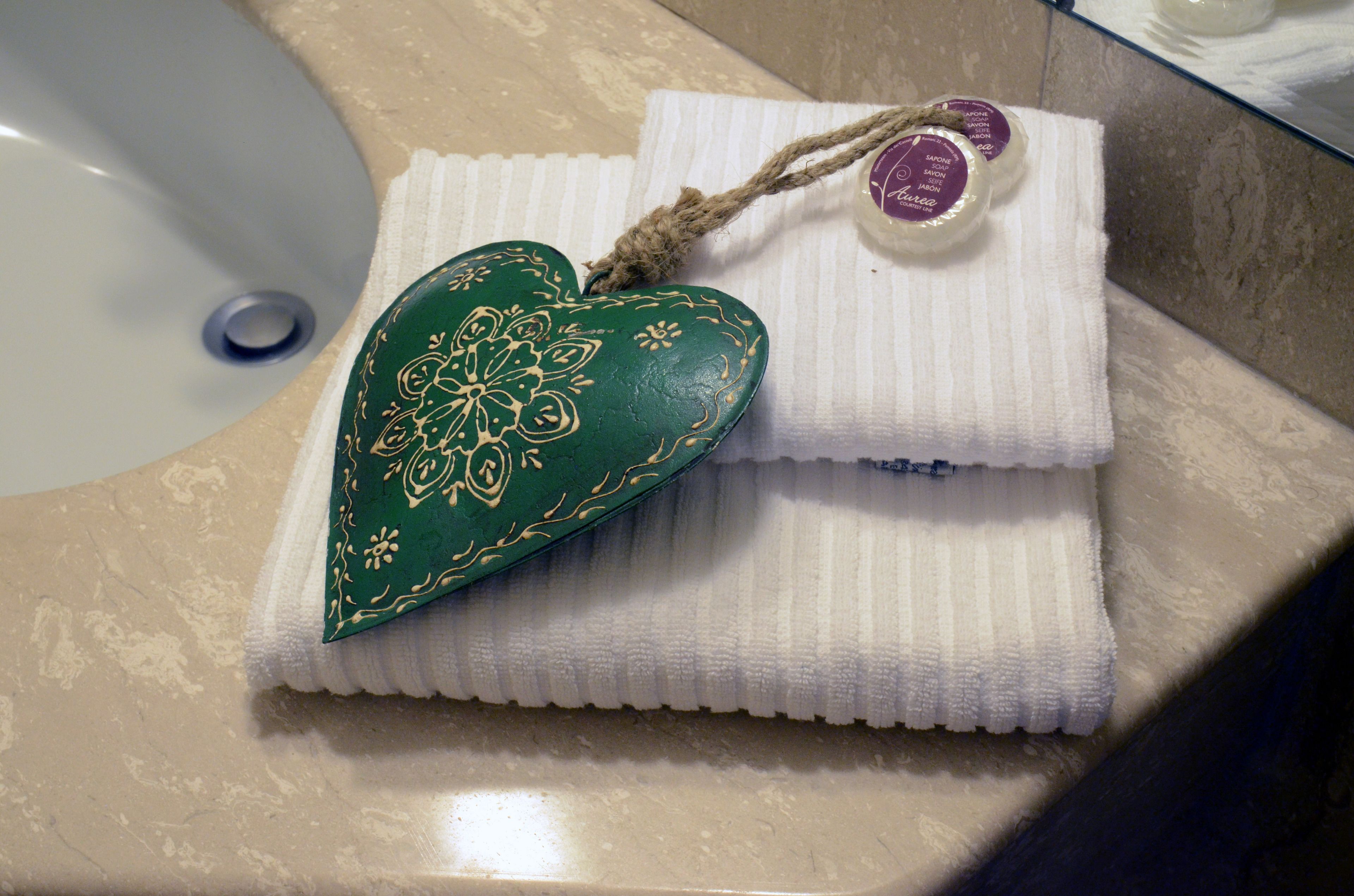 Un baño con un lavamanos blanco, un jabonera verde con forma de corazón y una toalla blanca con una pastilla de jabón morada.