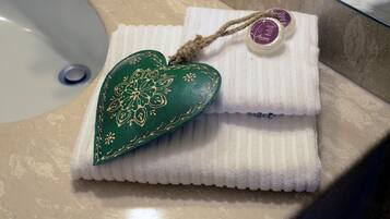 Un baño con un lavamanos blanco, un jabonera verde con forma de corazón y una toalla blanca con una pastilla de jabón morada.