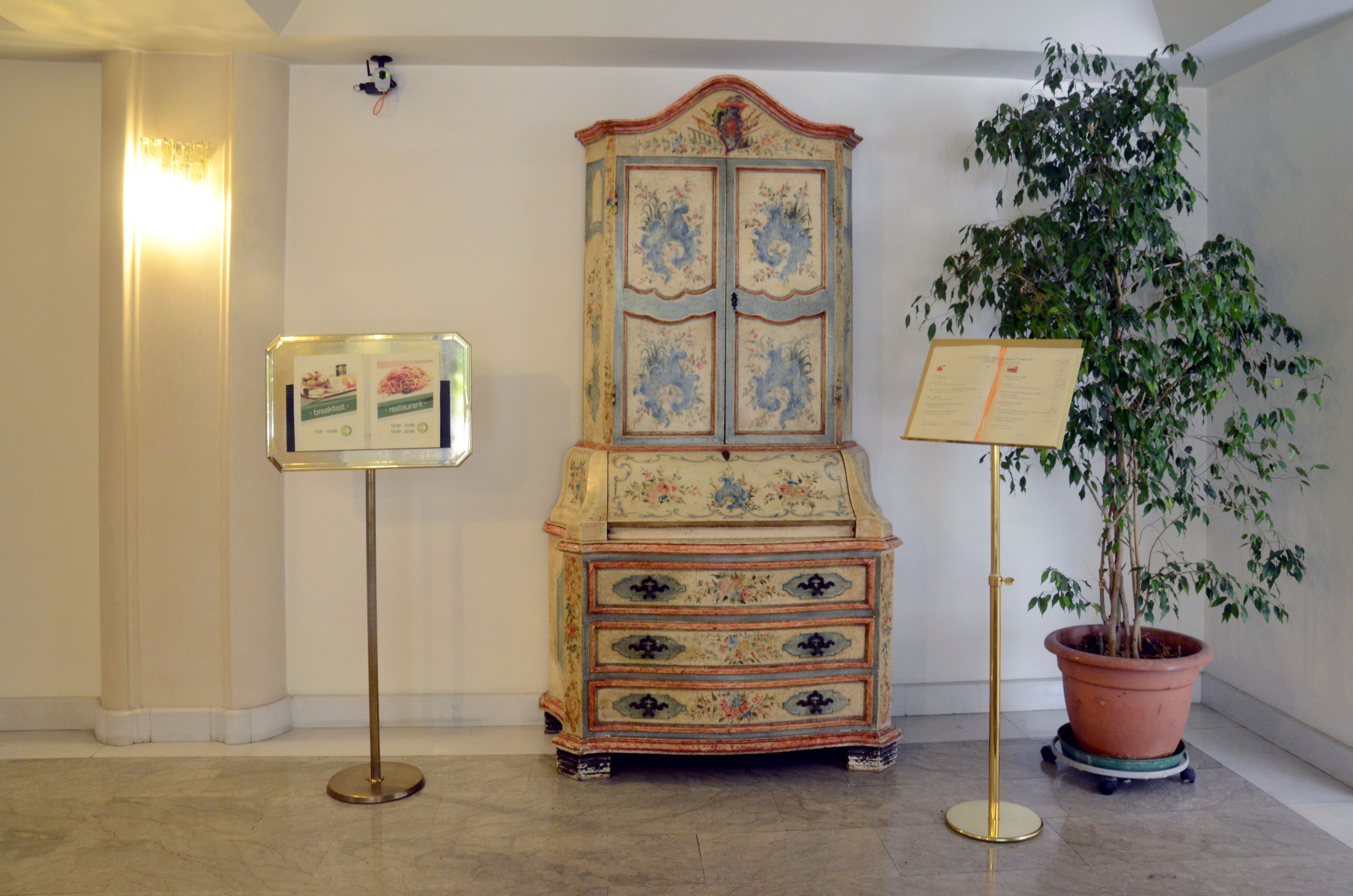 Ein Zimmer mit einer Kommode im Vintage-Stil, einer Topfpflanze und einer Vitrine für Informationskarten.
