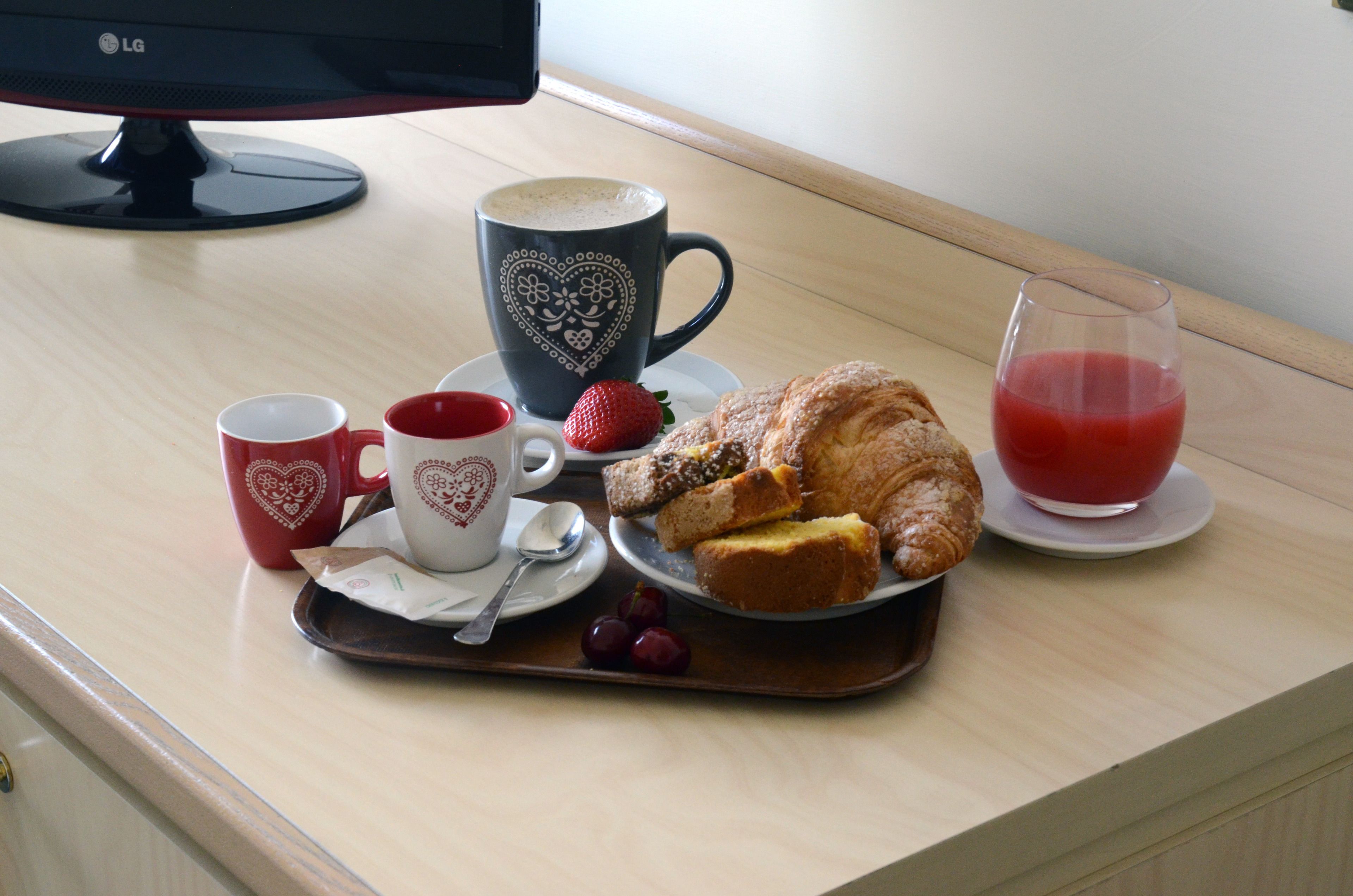 Un plateau de petit-déjeuner avec des viennoiseries, une tasse de café, un verre de jus de fruits et deux tasses sur une table en bois.