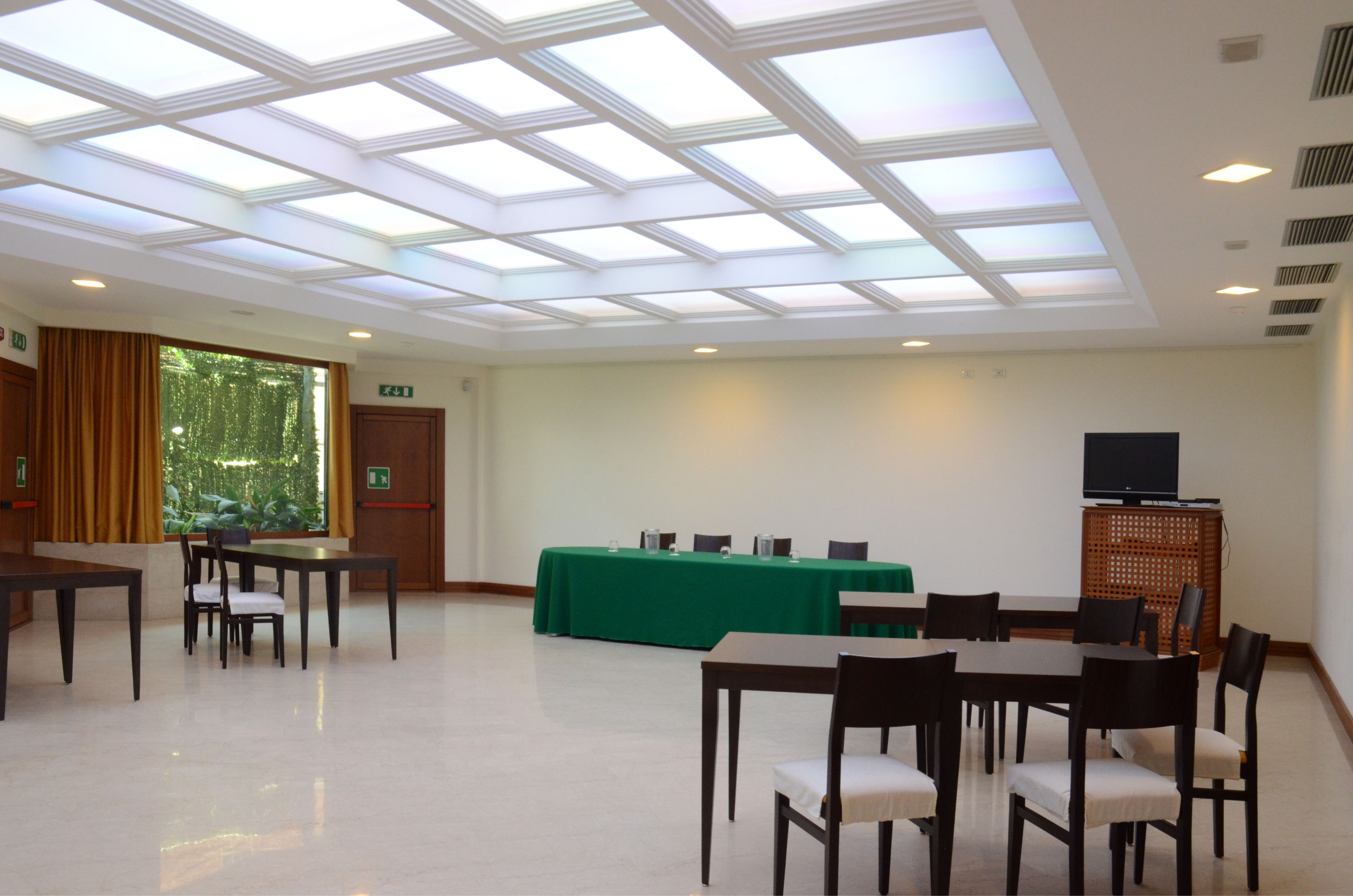 Ein Konferenzraum mit hoher Decke, Dachfenstern, einem grünen Tisch und mehreren Stühlen.