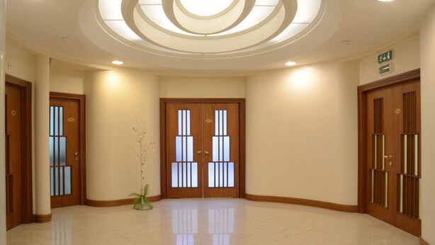 A spacious hallway with a skylight, wooden doors with vertical bars, and a potted plant. - Hotel Bassetto (Ferentino)