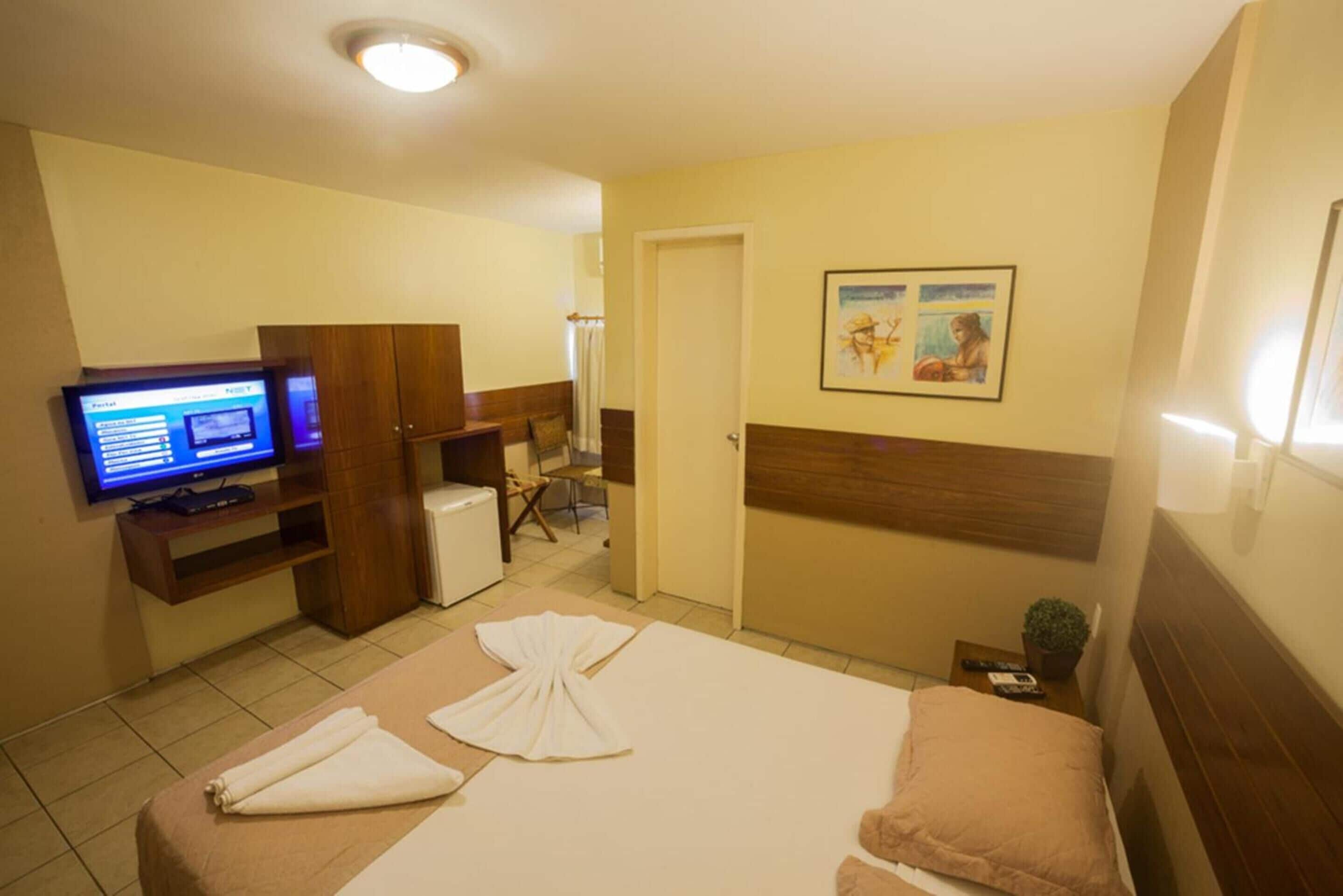 A hotel room with a bed, a desk with a computer, a television, and a door leading to a bathroom.