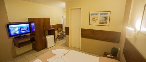 Une chambre d’hôtel comprenant un lit, un bureau avec un ordinateur, une télévision et une porte donnant sur une salle de bain.