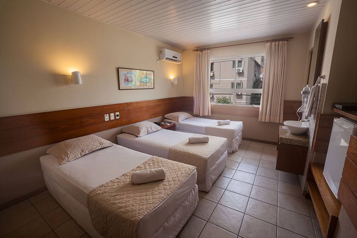 Quarto de hotel com duas camas, uma janela com cortinas, uma pia e um espelho.
