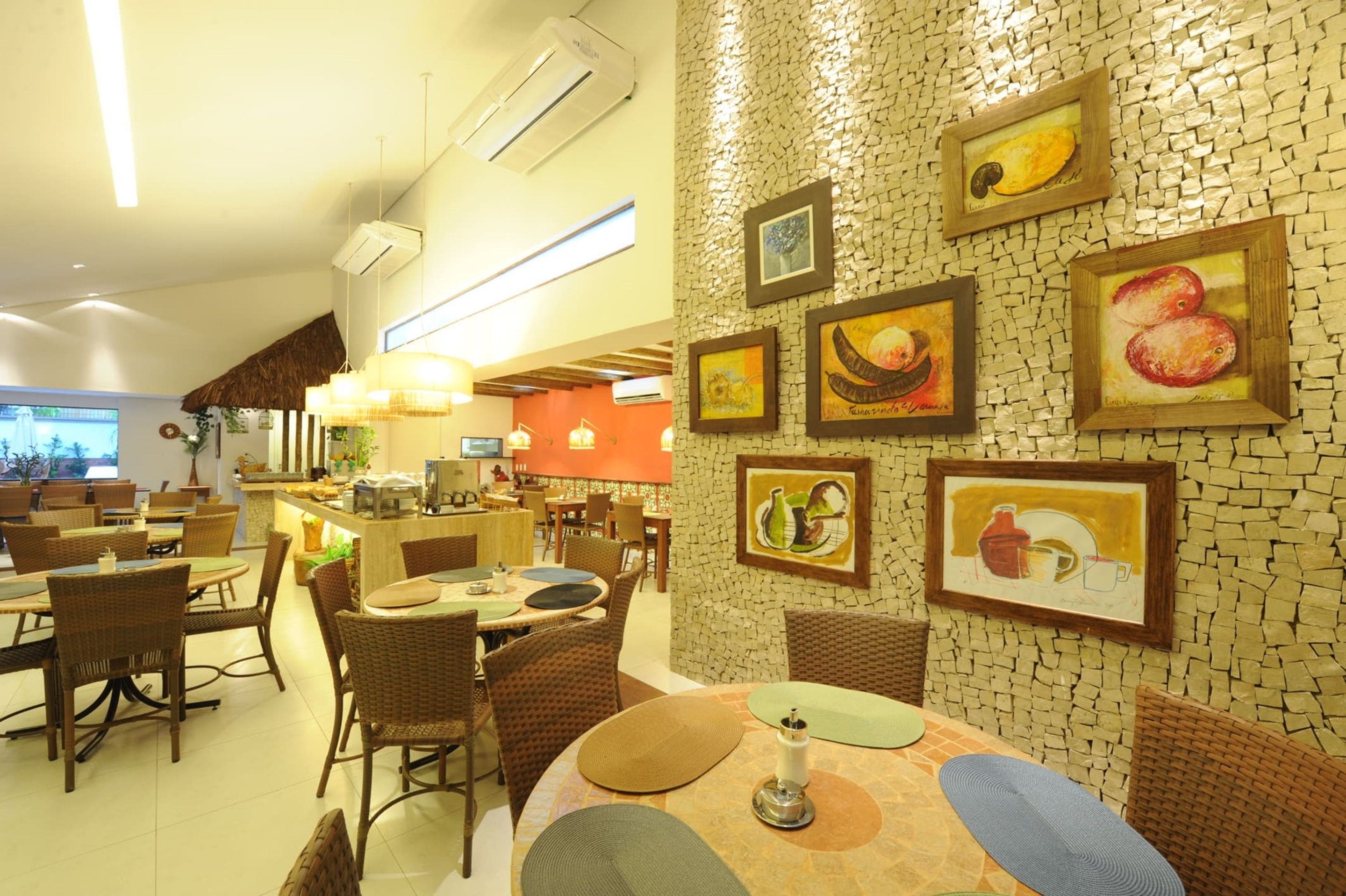 Un restaurante con mobiliario de mimbre, una pared con azulejos y obras de arte, y una zona de bar.