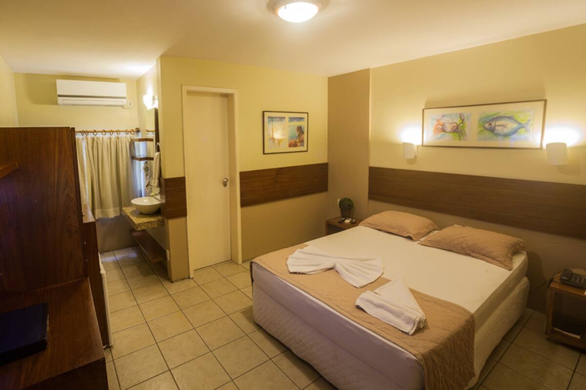 Quarto de hotel com cama, banheiro e escrivaninha.