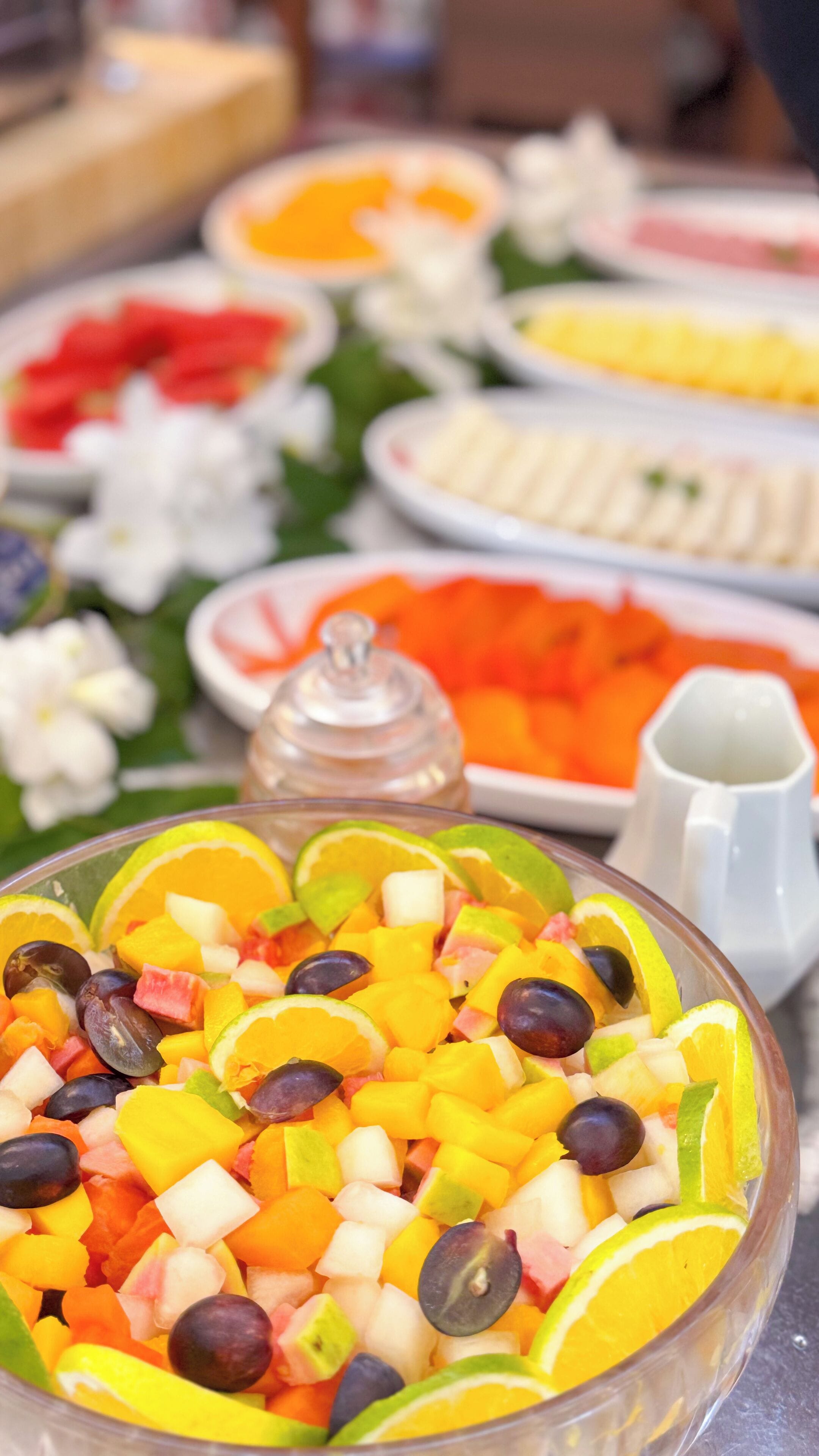 A buffet table with various dishes, including a bowl of mixed fruit salad in the foreground.