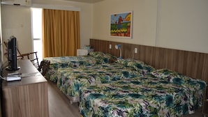 A hotel room with two beds, a desk with a computer and a lamp, a painting on the wall, and a window with curtains. - Hotel Casa de Praia (Fortaleza)