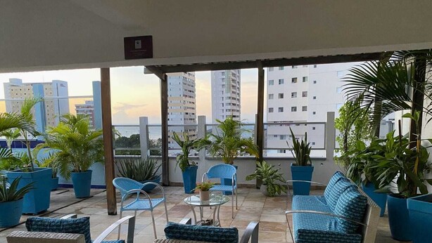 A covered outdoor seating area with wicker furniture and potted plants, overlooking a cityscape. - Hotel Casa de Praia (Fortaleza)