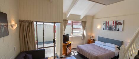 A room with a bed, a sofa, a television, and a window with curtains.