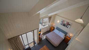 Une chambre à coucher avec un lit, une table de chevet, une lampe et une vue sur l’extérieur.