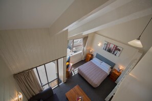 A bedroom with a bed, bedside table, lamp, and a view of the outside.