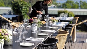 Une table à manger dressée avec des verres à vin, des assiettes et des fleurs, offrant une vue panoramique.