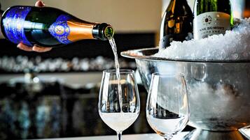 A bottle of champagne being poured into a glass, with another bottle and ice in the background.