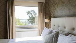 Une chambre d’hôtel avec un grand lit, une fenêtre avec des rideaux, une lampe et une vue sur la verdure.
