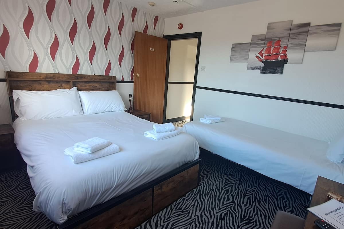 Quarto de hotel com uma cama grande, uma cama menor, uma cabeceira de madeira, um tapete com padrão de zebra e uma parede com arte abstrata.