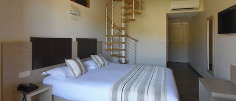 A hotel room with a bed, a desk, a chair, a phone, a TV, a wall-mounted air conditioner, and a spiral staircase.
