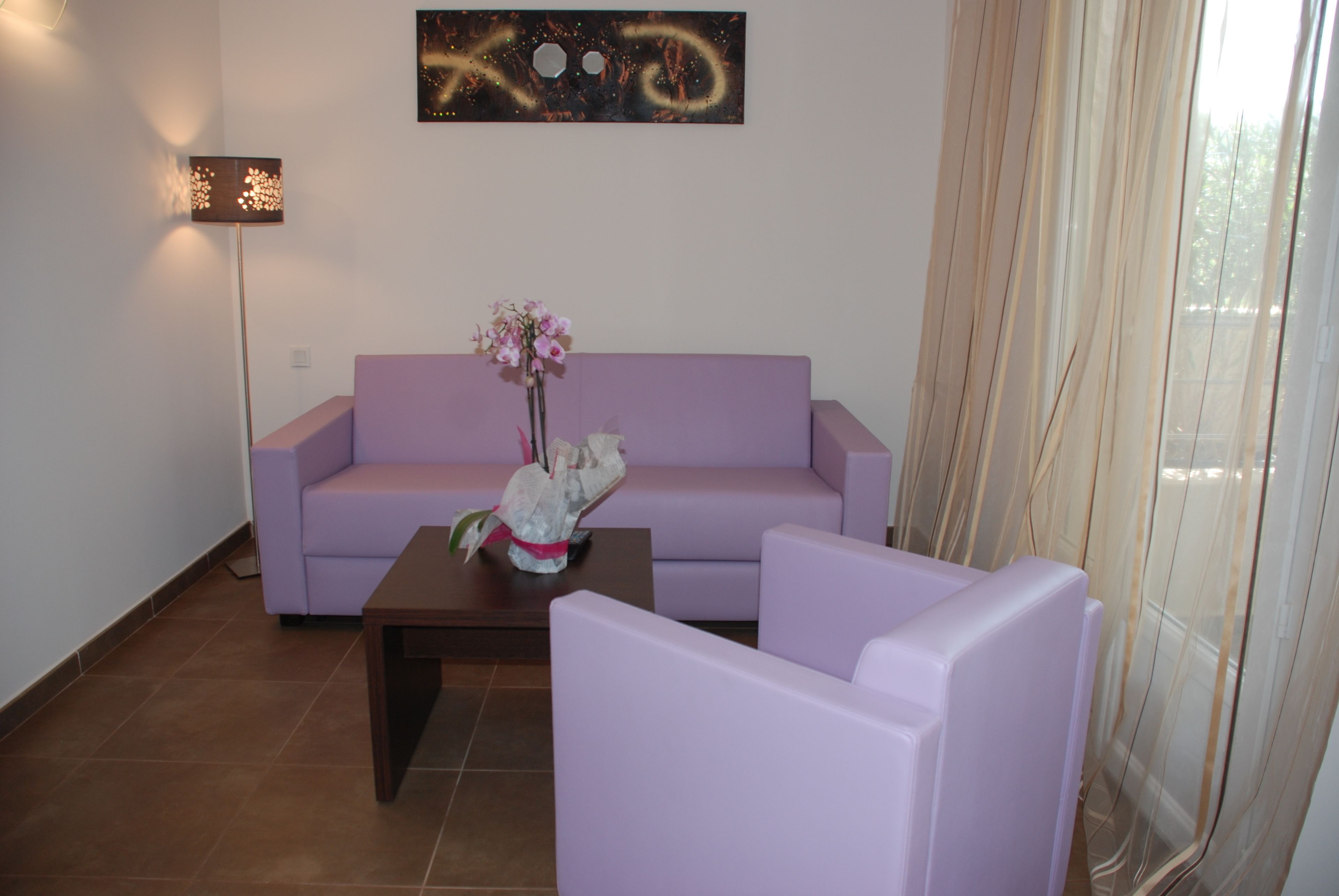 A living room with a purple sofa, a small table with a vase of flowers, and a floor lamp.