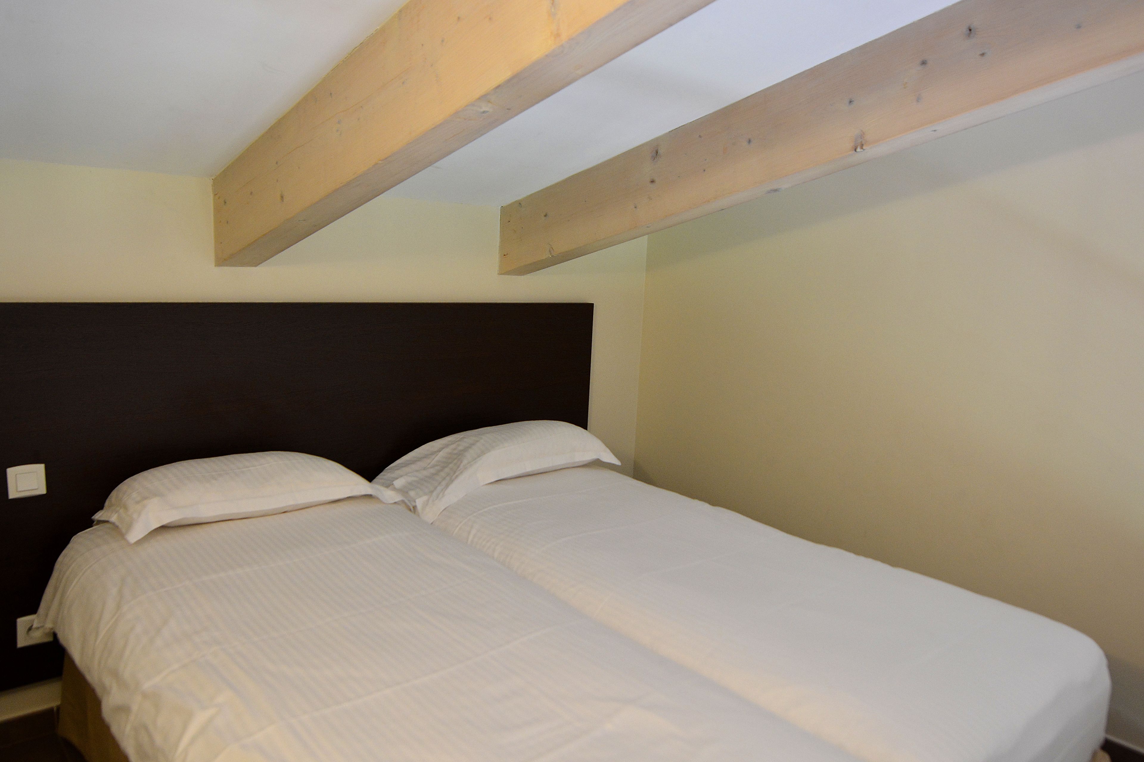 A single bed with a dark headboard in a room with exposed wooden beams.