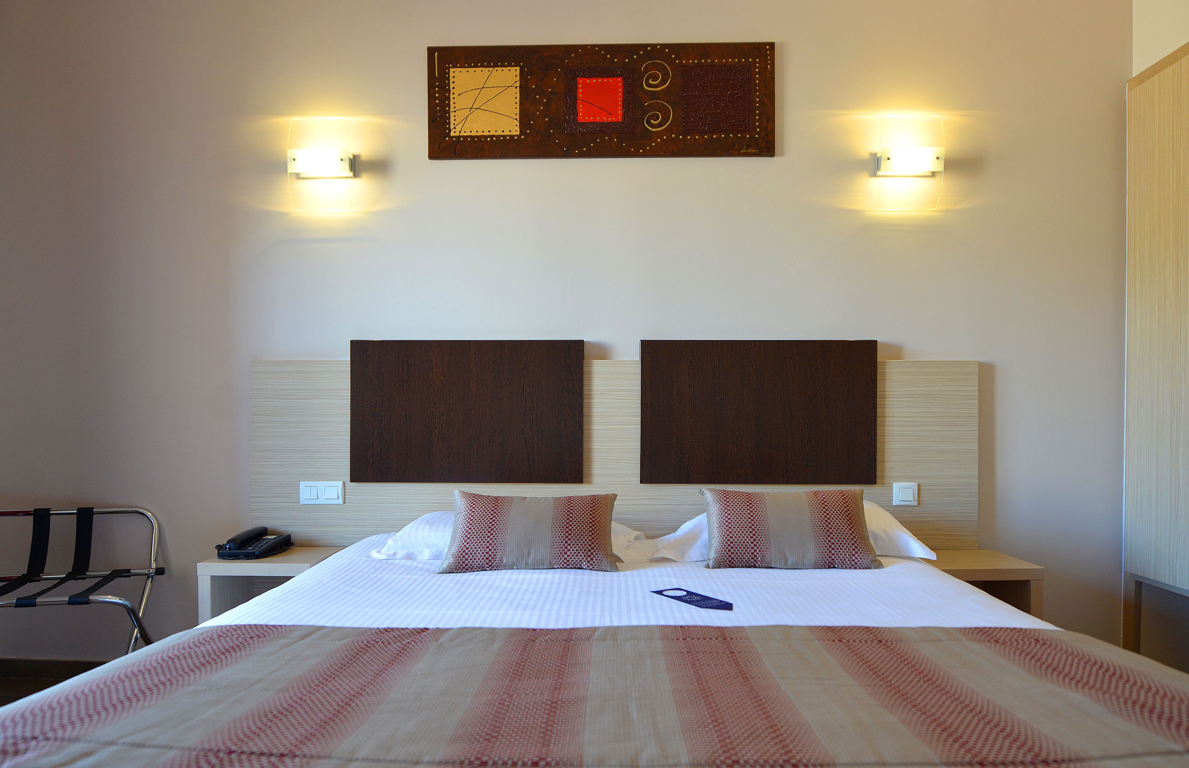 A hotel room with a large bed, two bedside tables, a nightstand, a chair, and a wall-mounted artwork.