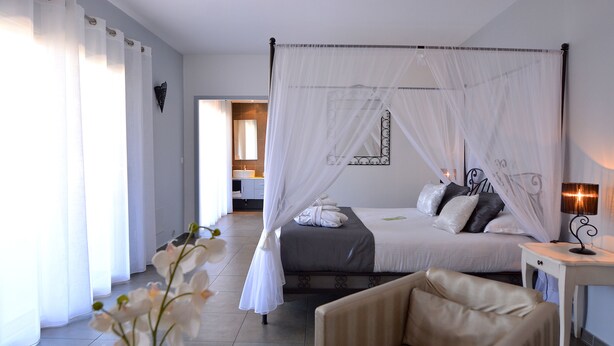 Een slaapkamer met een hemelbed, een nachtkastje, een stoel en een spiegel aan de muur.