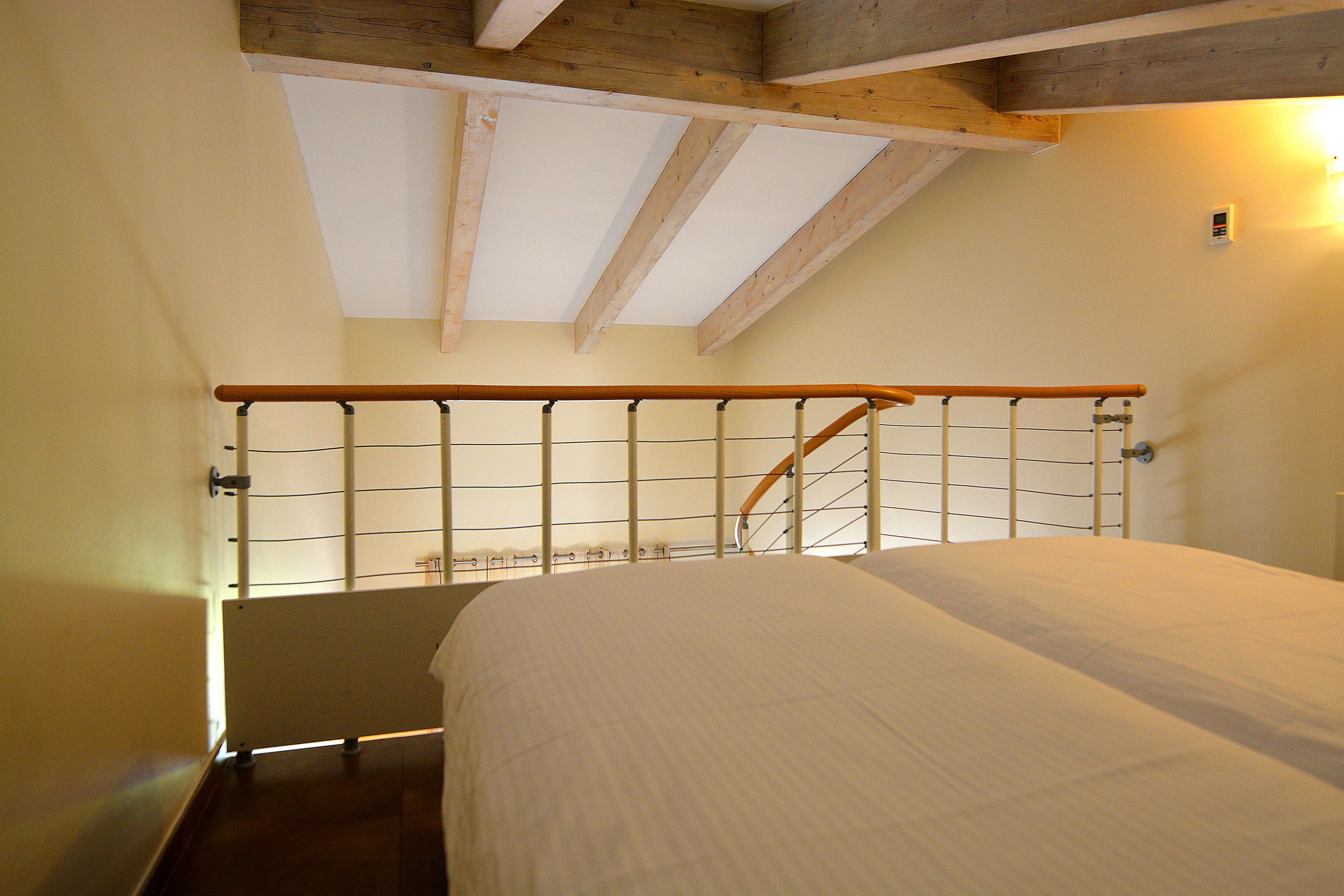 Ein Schlafzimmer mit Holzboden, einem Bett und einem Fenster mit Blick auf einen Balkon.