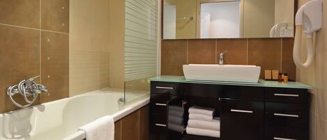 Un baño moderno con bañera de hidromasaje con mampara de vidrio, un lavabo blanco y un mueble de tocador negro con cajones.