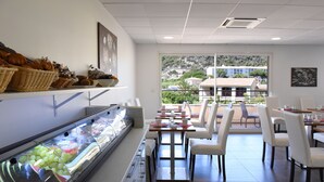 Een buffetgedeelte met diverse soorten eten, waaronder fruit en gebak, en een zithoek met tafels en stoelen.