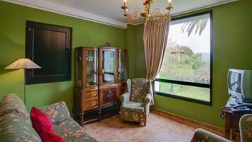 A room with a green wall, a wooden cabinet, a floral armchair, a sofa with a red pillow, and a television on a wooden table.