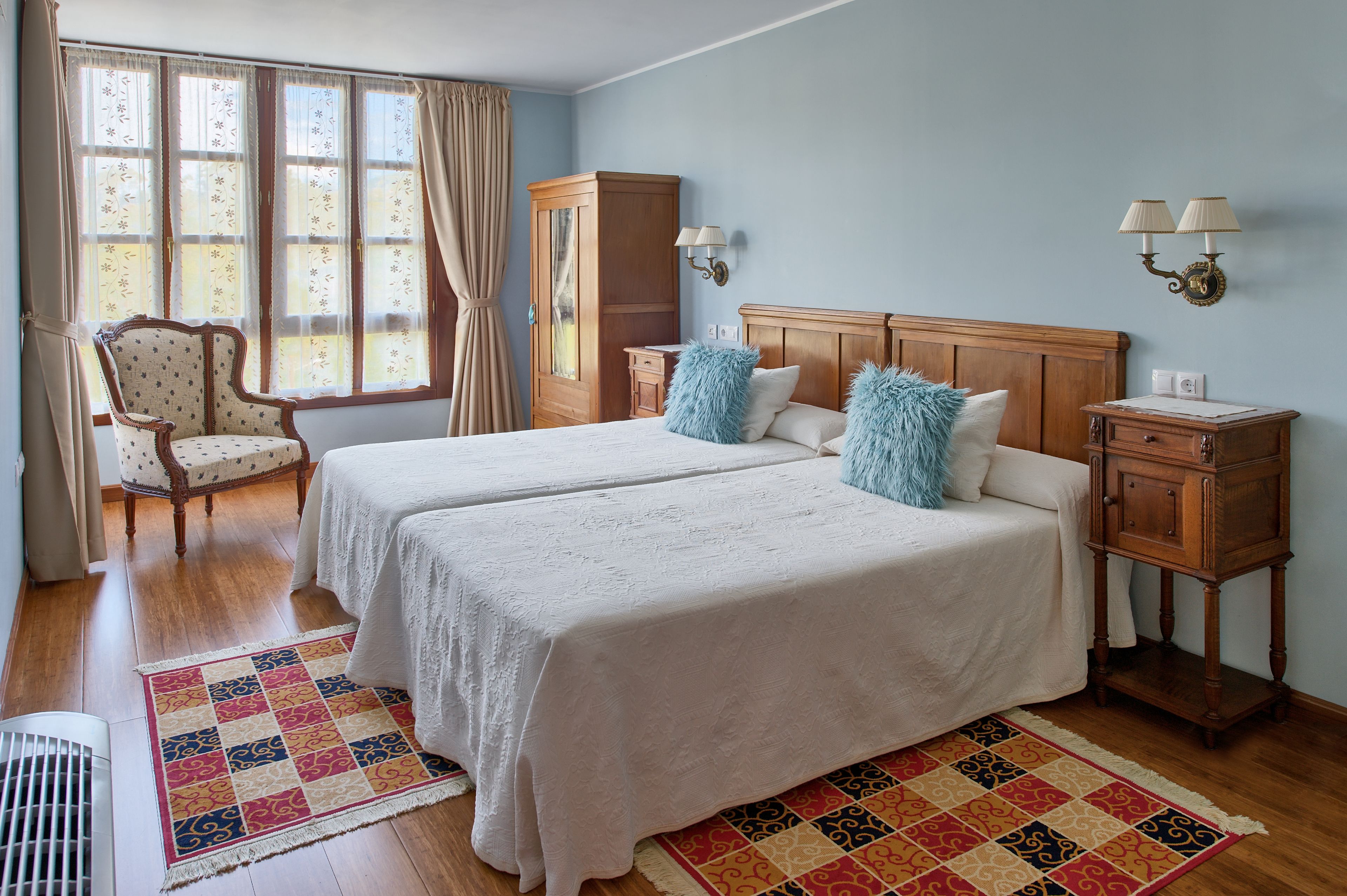 A hotel room with two beds, a chair, a wardrobe, a nightstand, and a window with curtains.