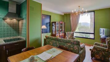Un comedor con una mesa de madera, sillas tapizadas con motivos florales, una araña y vistas a través de una ventana.