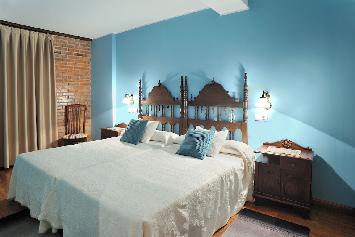 Een slaapkamer met een groot bed, een bakstenen muur, een houten hoofdeinde en een nachtkastje met een lamp.