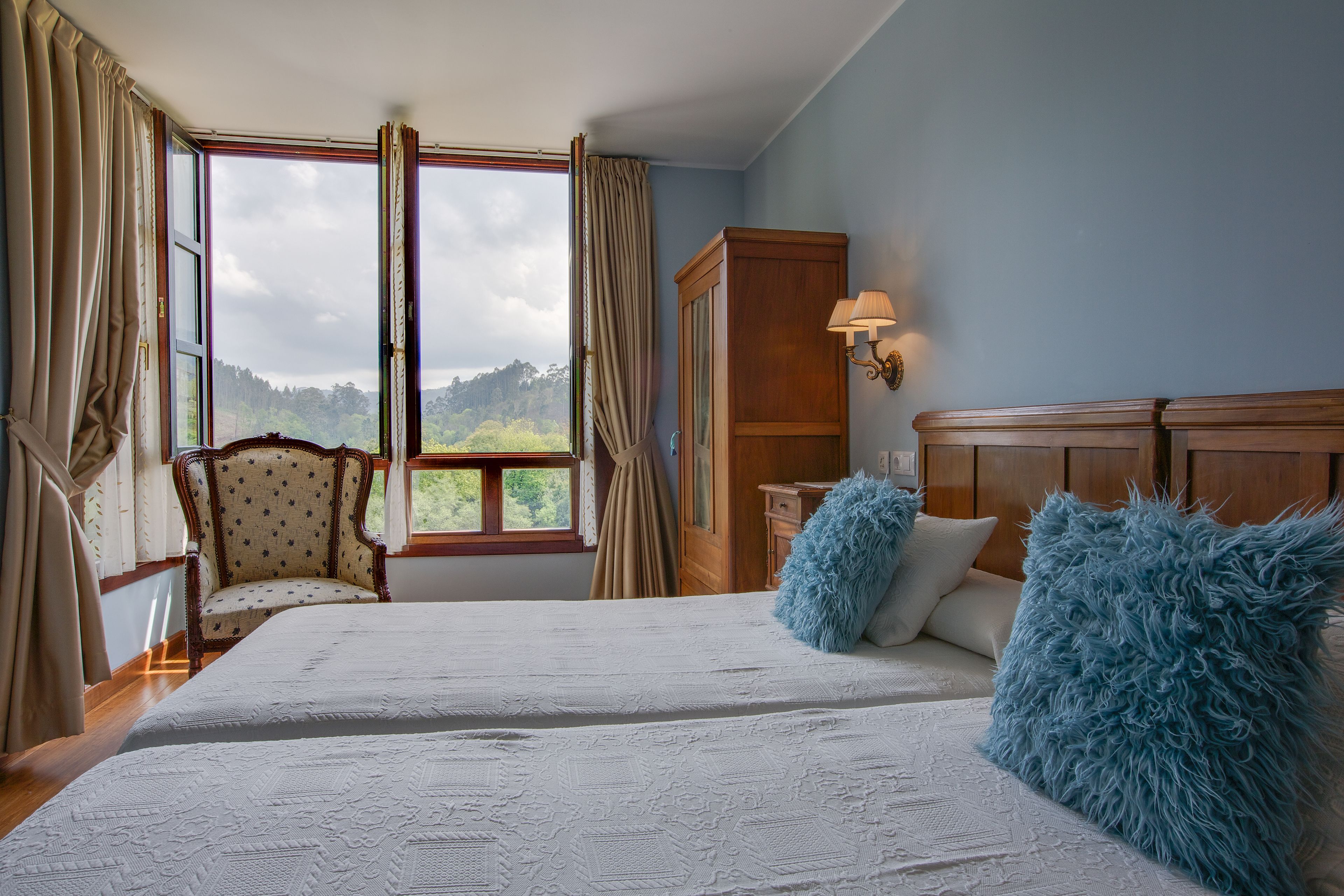 Een slaapkamer met een groot bed, een stoel, een kast en een raam met gordijnen.