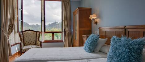 A bedroom with a large bed, a chair, a wardrobe, and a window with curtains.
