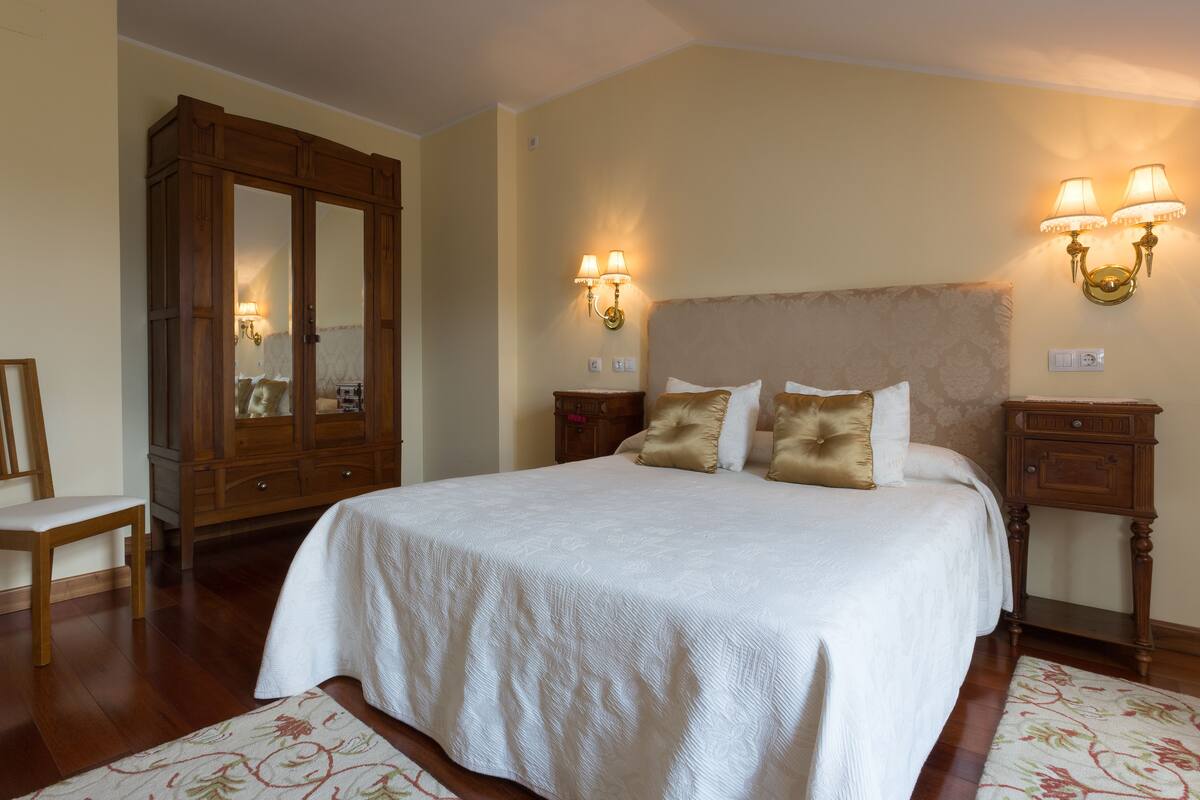 Une chambre à coucher avec un grand lit, une armoire en bois, deux tables de chevet avec des lampes, une chaise et un tapis à motifs.
