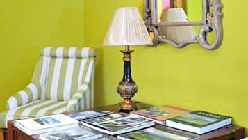 Una habitación con pared verde, un escritorio de madera con libros, una lámpara, una silla a rayas y un espejo.