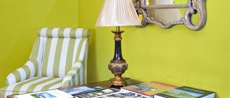 A room with a green wall, a wooden desk with books, a lamp, a striped chair, and a mirror.