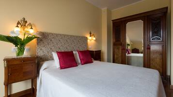 A neatly made bed with white and red pillows, a floral headboard, and a bedside table with a vase of flowers.