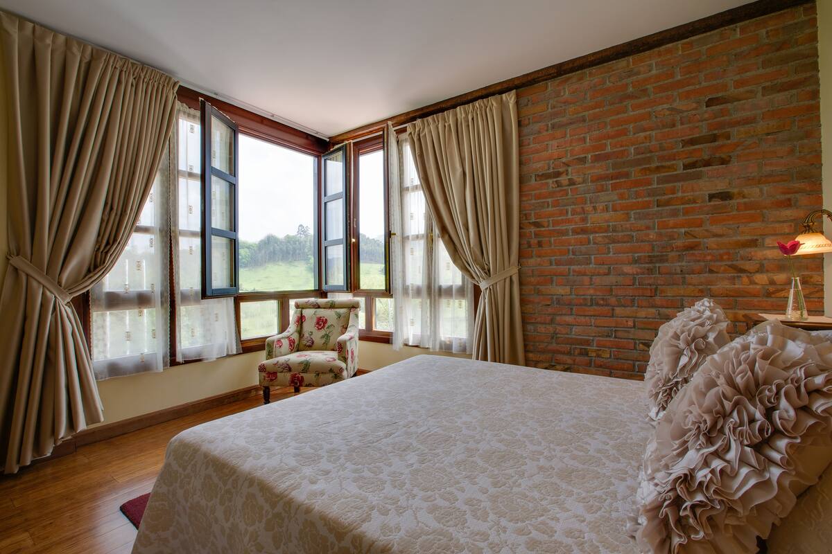 Une chambre avec un grand lit, une chaise et un mur en briques.