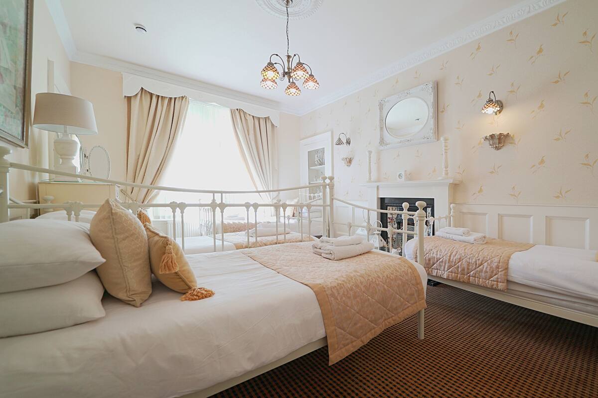 A hotel room with two beds, a chandelier, a mirror, and a fireplace.