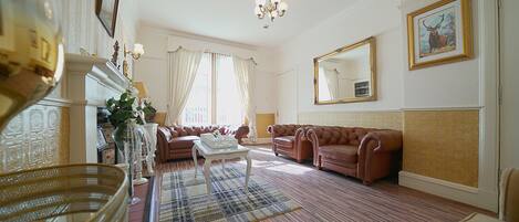 A spacious living room with a large brown leather sofa, a white coffee table, and a patterned rug.
