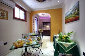 Un comedor con una mesa lista para el desayuno, una cocina al fondo y un cuadro en la pared.