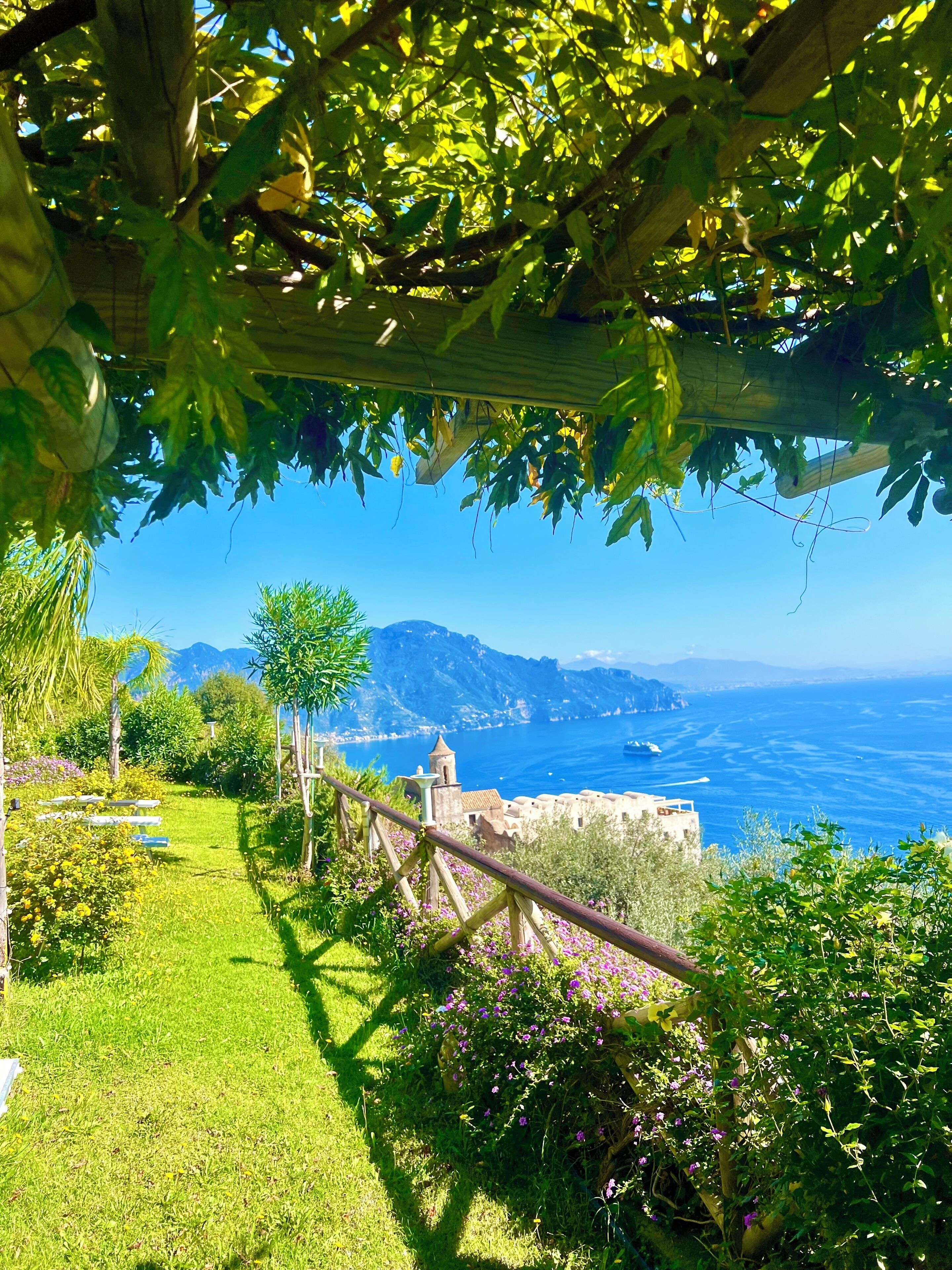 A garden with a pergola, a pathway, and a view of the sea and mountains.