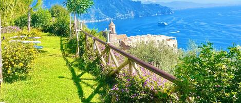 A garden with a pergola, a pathway, and a view of the sea and mountains.