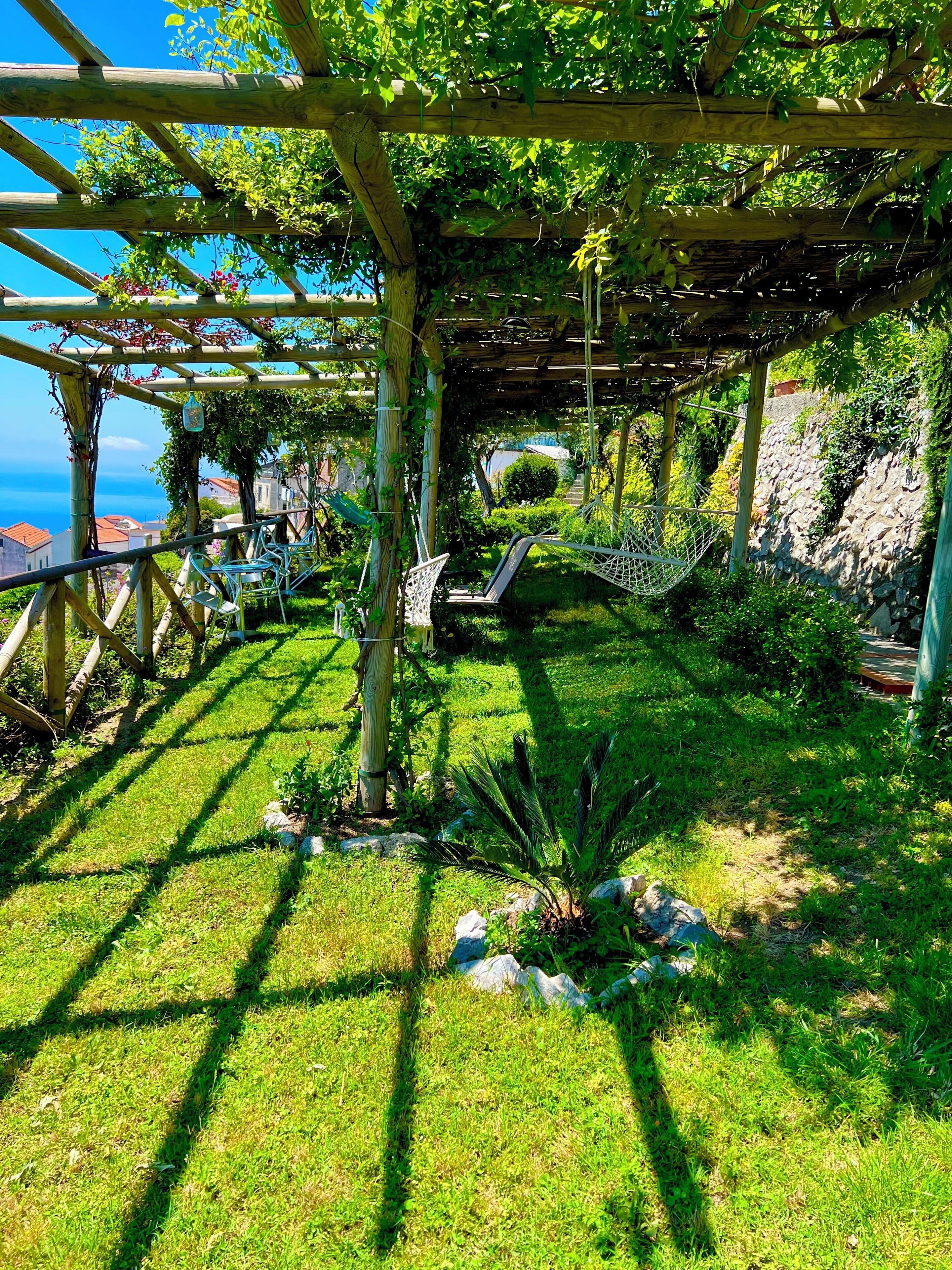Een tuin met een pergola, een zitgedeelte en uitzicht op zee.