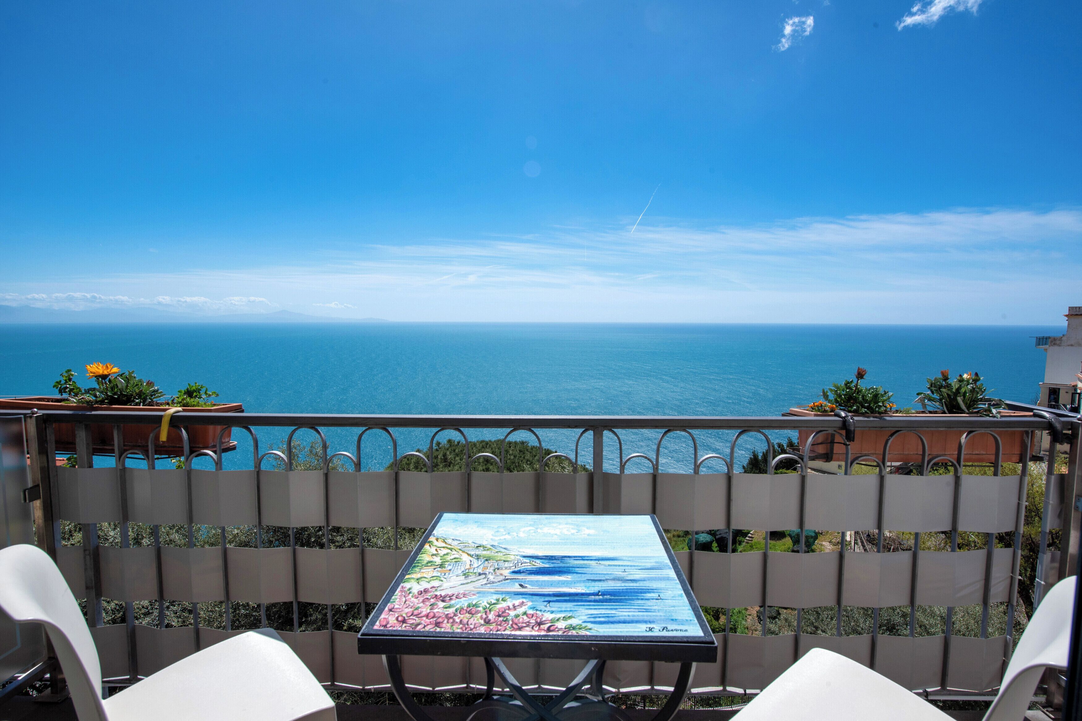 A balcony with a table and chairs overlooking the sea.