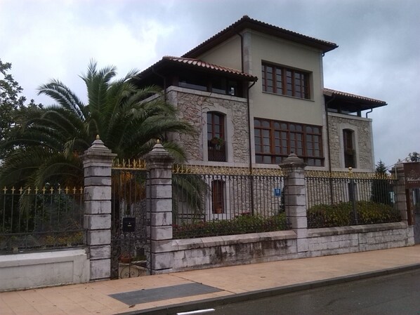 A two-story building with a stone facade, large windows, and a gated entrance. - Hotel Villadesella (Ribadesella)