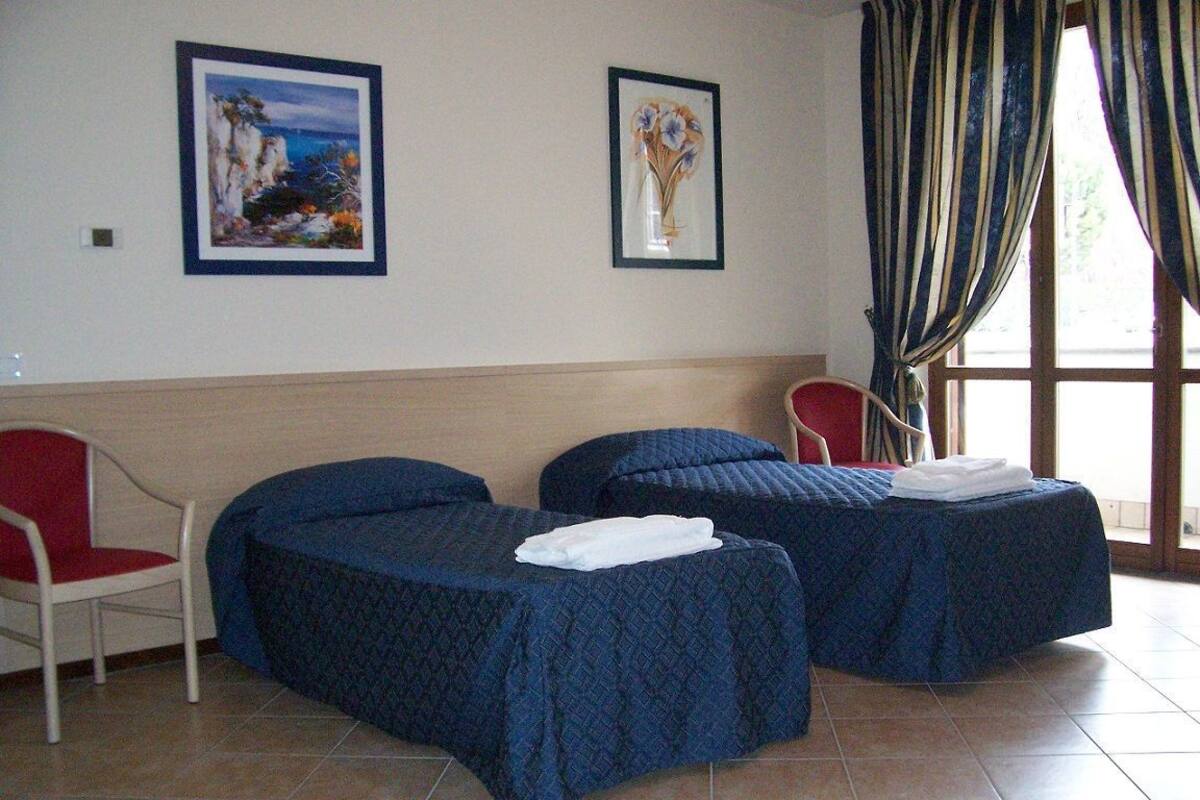 A hotel room with two beds, a red chair, and two framed artworks on the wall.