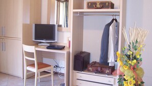A room with a wooden desk, a television, a wardrobe with hanging clothes, and a vase with flowers. - Villa Giovanna (Somma Lombardo)